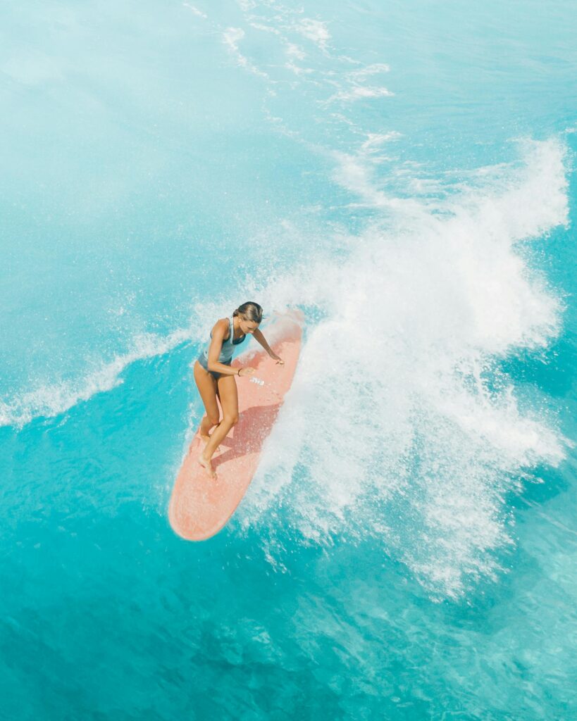 pexels-photo-4321800-4321800 Aerial view of a female surfer skillfully riding waves on a vibrant turquoise ocean.