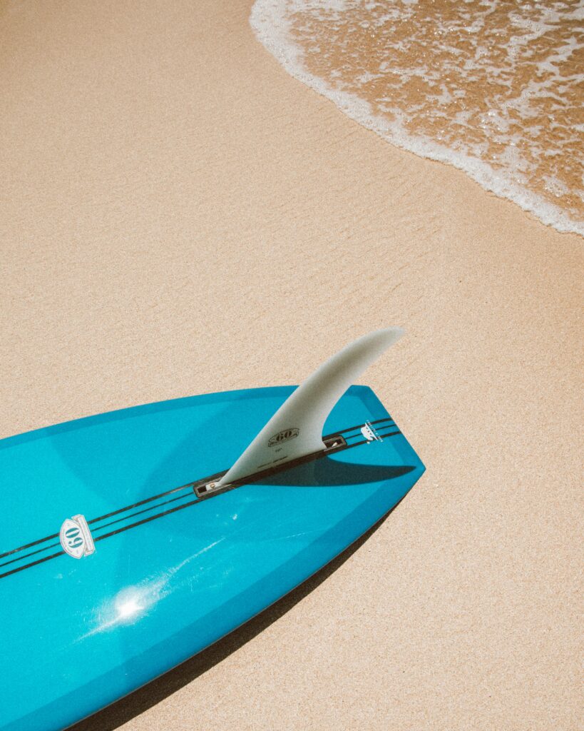 pexels-photo-4603866-4603866 Blue surfboard resting on a sandy beach in Hawaii, capturing a perfect beach day.
