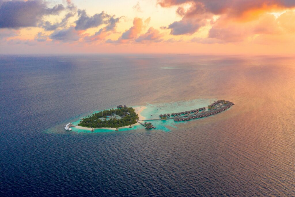 A picturesque aerial view of a tropical island resort surrounded by clear blue ocean during a vibrant sunset.